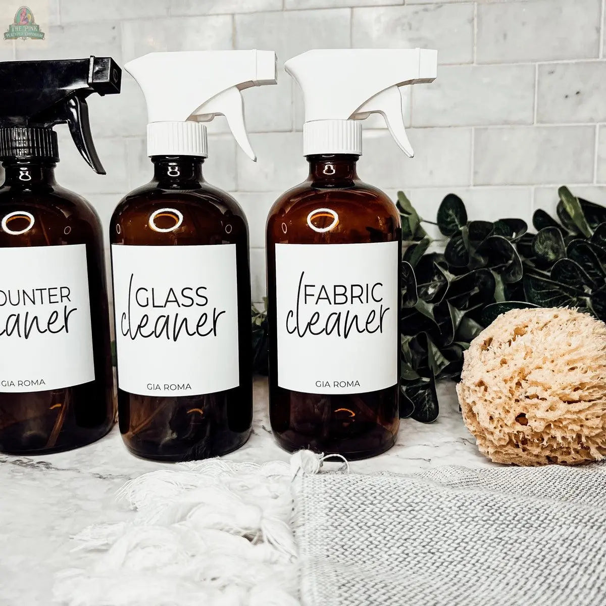 16oz Glass Cleaning Bottles with white labels are ideal as refill bottles or a stylish glass dispenser for your cleaning routine, shown next to a sponge.