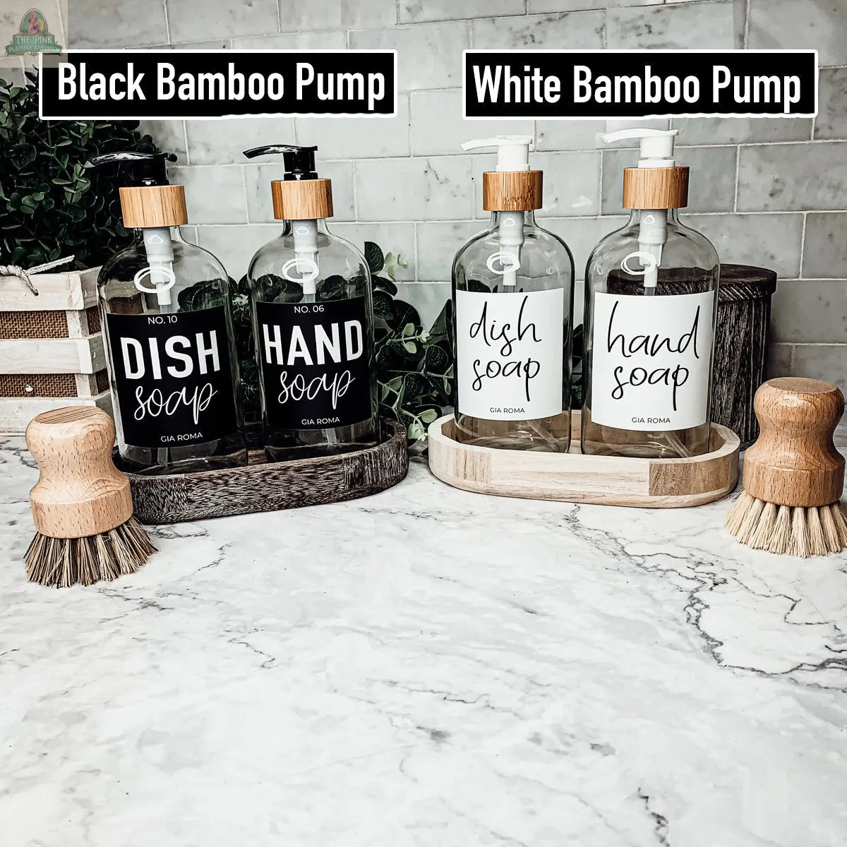 Two sets of "16oz Glass Clear | White Label" bottles, labeled “Dish Soap” and “Hand Soap,” sit on a marble counter. One set features black bamboo pumps, the other white; wooden scrub brushes rest beside each set.