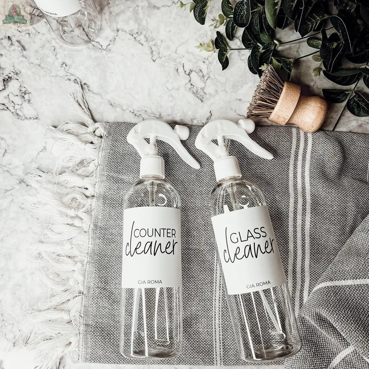 16oz Plastic Cleaning Bottles with waterproof labels are placed on a towel beside a plant.