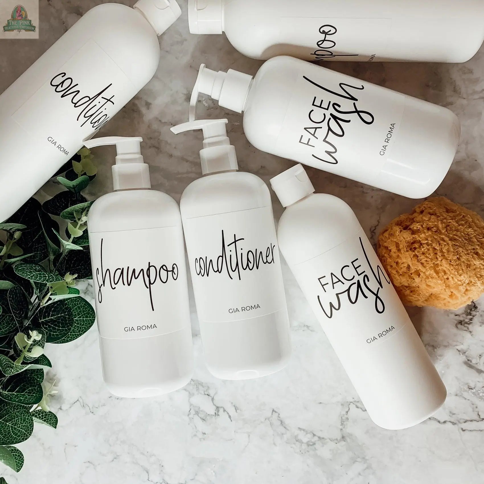The 16oz Plastic White bottles with handwritten-style white waterproof labels are arranged on marble with a yellow sponge and green leaves, adding a modern, stylish touch to these refillable dispensers.