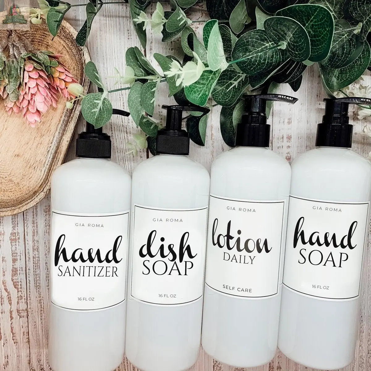 Four 16oz Plastic White | White Label bottles are lined up on a rustic wooden surface with green leaves and pink flowers beside them, each featuring a refillable dispenser and waterproof label.