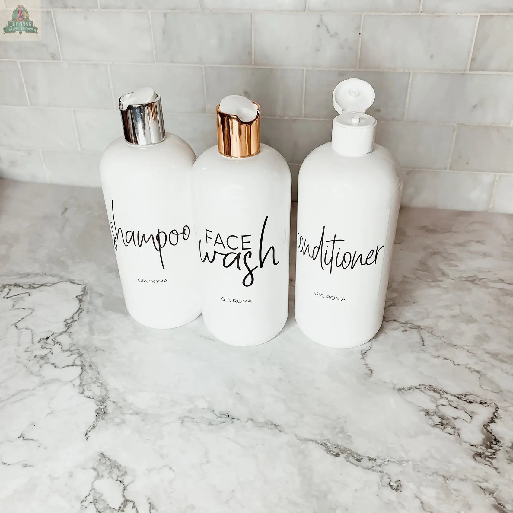 Three 16oz Plastic White | White Label bottles, labeled shampoo, face wash, and conditioner, rest on a marble countertop. Each refillable dispenser features a silver, rose gold, or white pump or flip-top lid with waterproof labels.