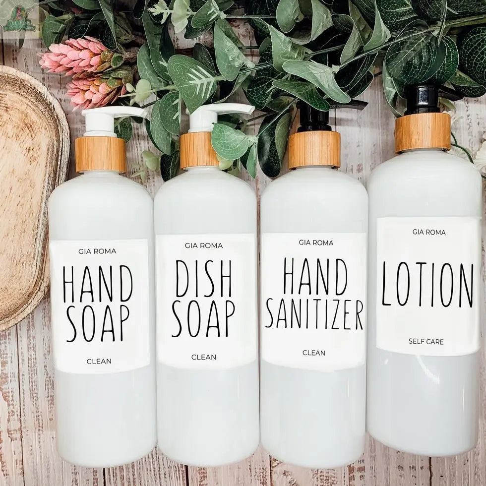 Four 16oz Plastic White | White Label bottles with wooden pump tops—labeled for Hand Soap, Dish Soap, Hand Sanitizer, and Lotion—sit on a light wood surface surrounded by refillable dispensers and green leafy plants.