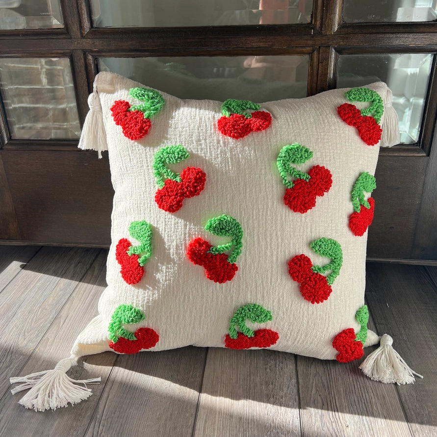 Decorative pillow with red and green cherry patterns on a wooden floor.
