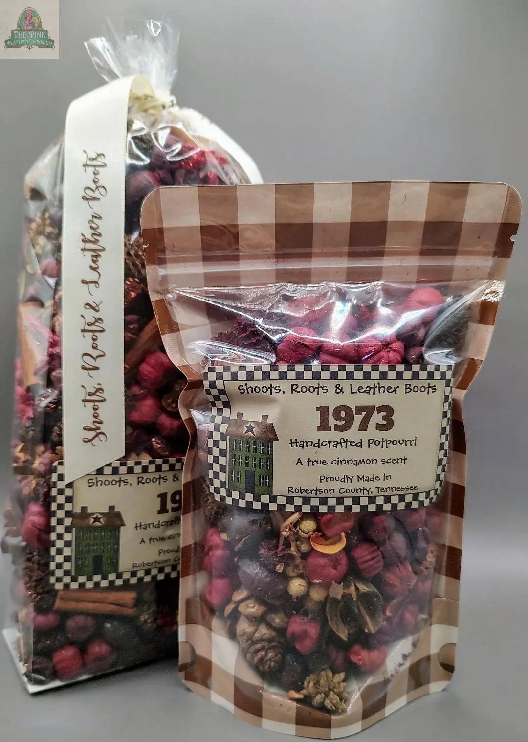 Two clear packages of "1973" (A True Cinnamon Scent) Handcrafted Potpourri, featuring dried botanicals in red, pink, and brown tones. Labels show decorative text and a small building illustration.