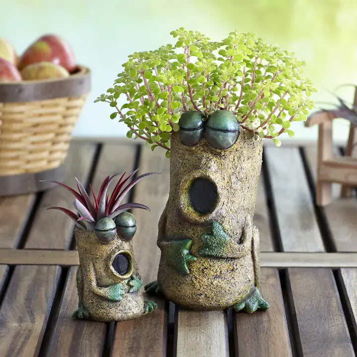 Two frog-shaped planters with plants on a wooden surface