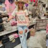 Person wearing a graphic t-shirt with text on it saying "don't squat with your spurs on" and jeans in a store setting