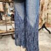 Blue jeans with fringe details on a wooden floor.