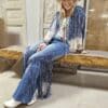 Person sitting on a wooden bench wearing a blue  jeans with fringe on the sides 