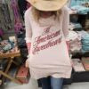 Person wearing a graphic t shirt that says "all american sweetheart" in an indoor setting