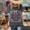 woman in cowboy had in a clothing store wearing boho style tshirt with "unapologetically girly" printed on it