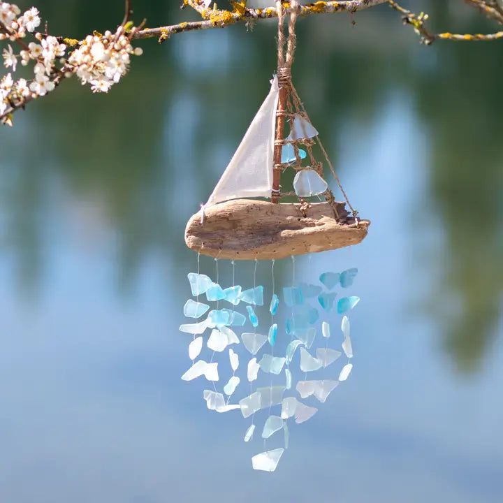 Decorative sailboat glass wind chime with sea glass on a branch against a blurred natural background