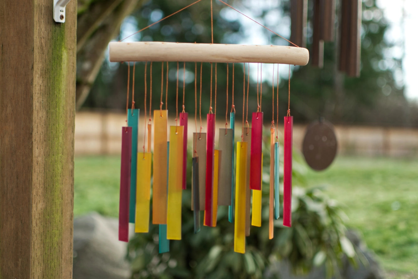 Colorful wind chime hanging on a wooden post with a garden background
