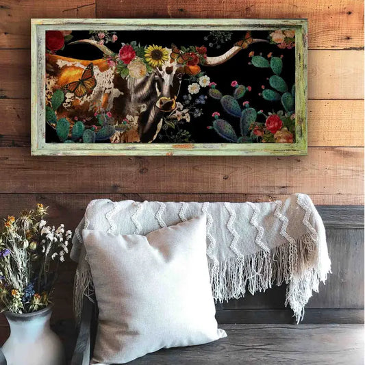Western wall art of a longhorn bull cow with flowers and cacti on a wooden wall above a sofa.