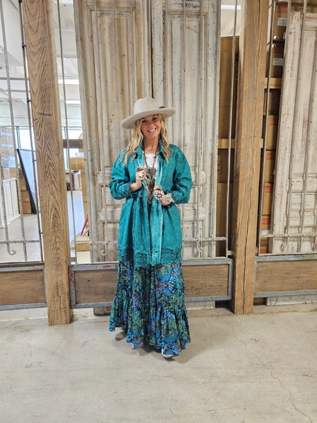 Woman in teal jacket and Peacock Feather Boho Pants standing in a room with wooden panels.