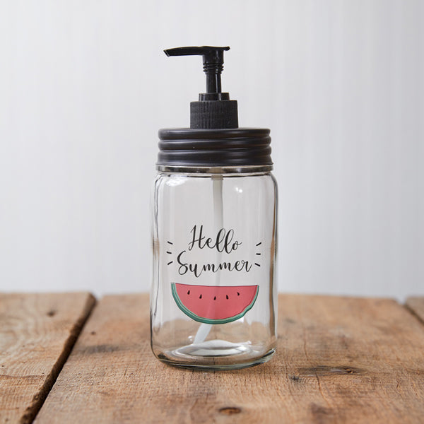 Glass dispenser with black pump and 'Hello Summer' label on a wooden surface