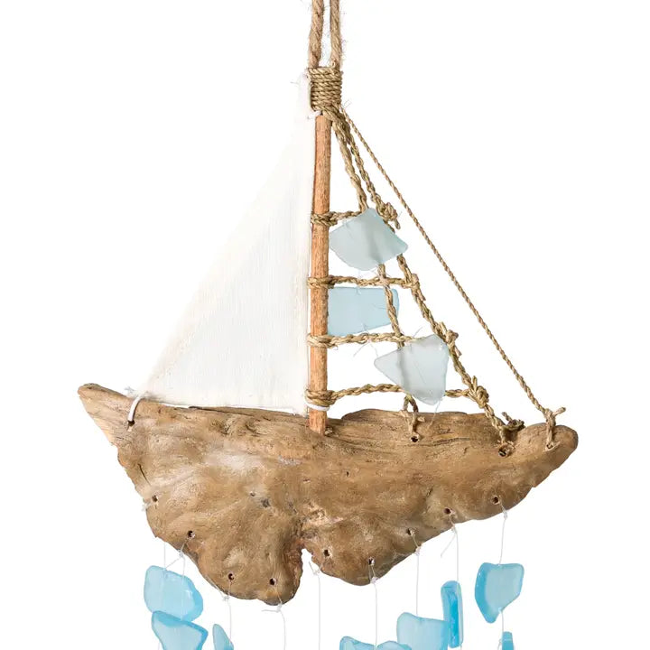 Decorative sailboat wind chime made from driftwood with a white sail and blue sea glass on a white background