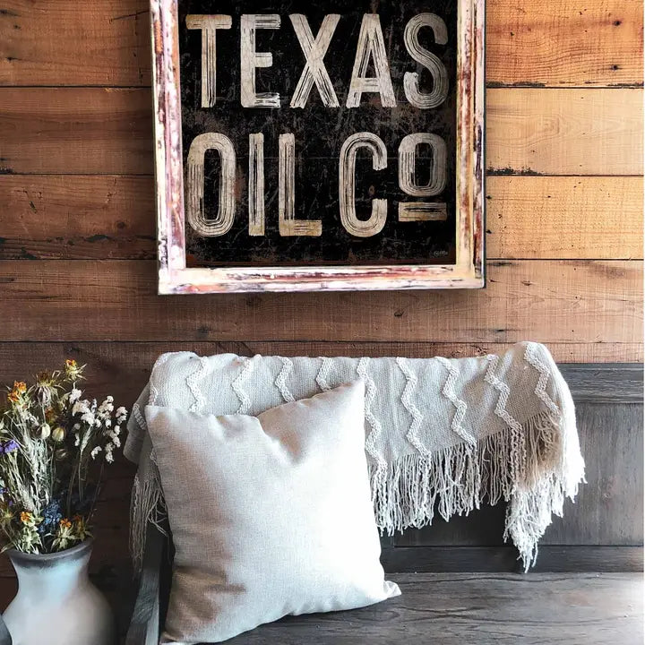 Decorative sign with 'Texas Oil Co' on a wooden wall above a couch with pillows and a blanket.