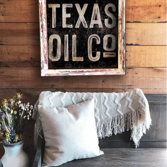 Decorative sign with 'Texas Oil Co' on a wooden wall above a couch with pillows and a blanket.