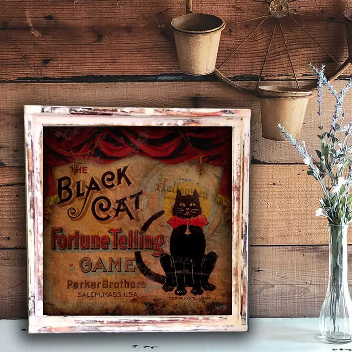 Vintage-style framed poster of 'The Black Cat Fortune Telling Game' by Parker Brothers on a wooden wall.
