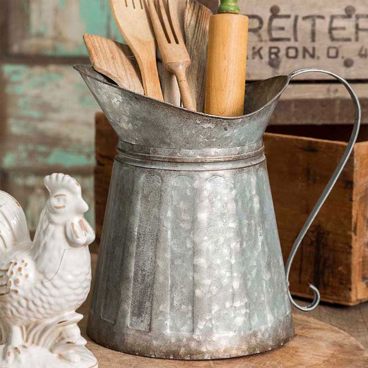 Vintage-style metal pitcher with wooden utensils against a rustic background