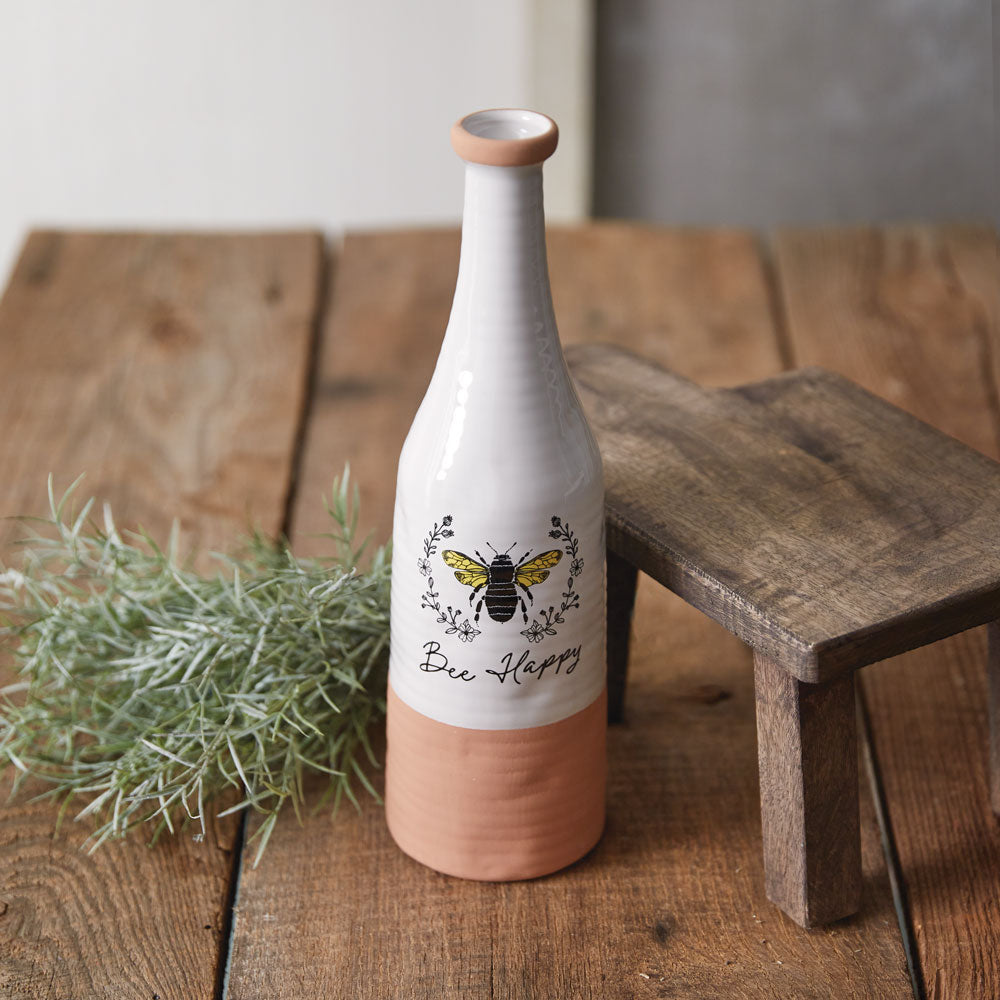 Decorative bottle with 'Bee Happy' text and a bee design on a wooden surface.