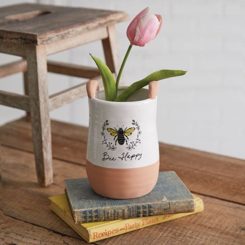 Vase with a pink tulip on top of books, featuring a bee design and 'Bee Happy' text.