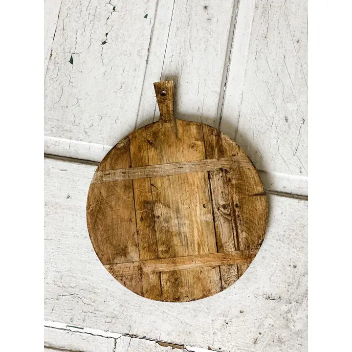 Round wooden cutting board with handles on a white wooden surface