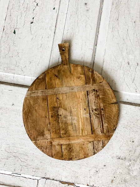 Round wooden cutting board with handles on a white wooden surface