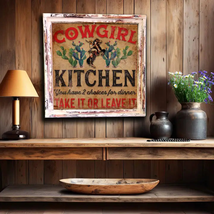Decorative sign with 'Cowgirl Kitchen' text on a wooden wall above a shelf.