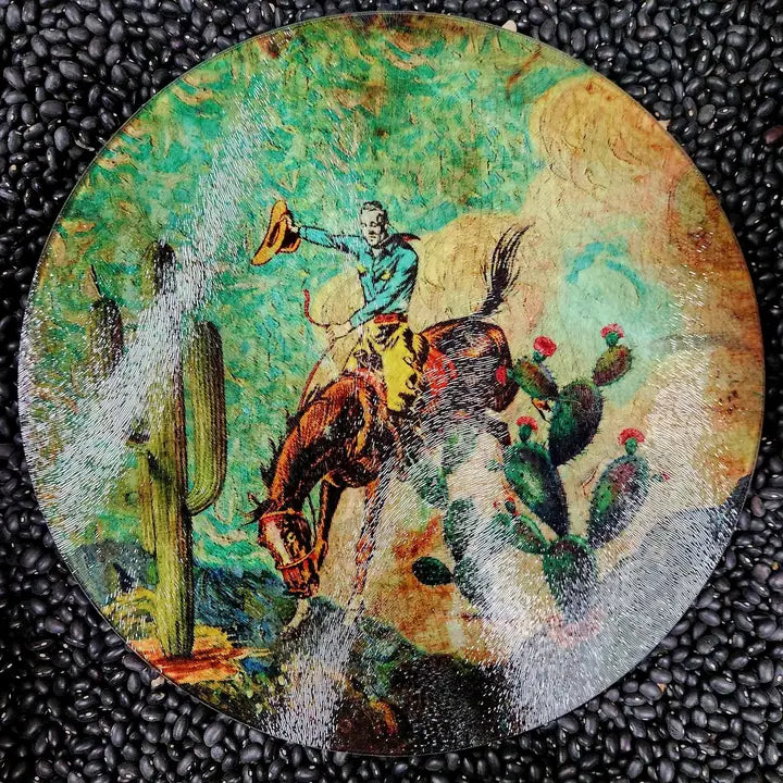 Round glass charcuterie board depicting a cowboy on horseback with cacti, on a textured black surface. - unique housewarming gift