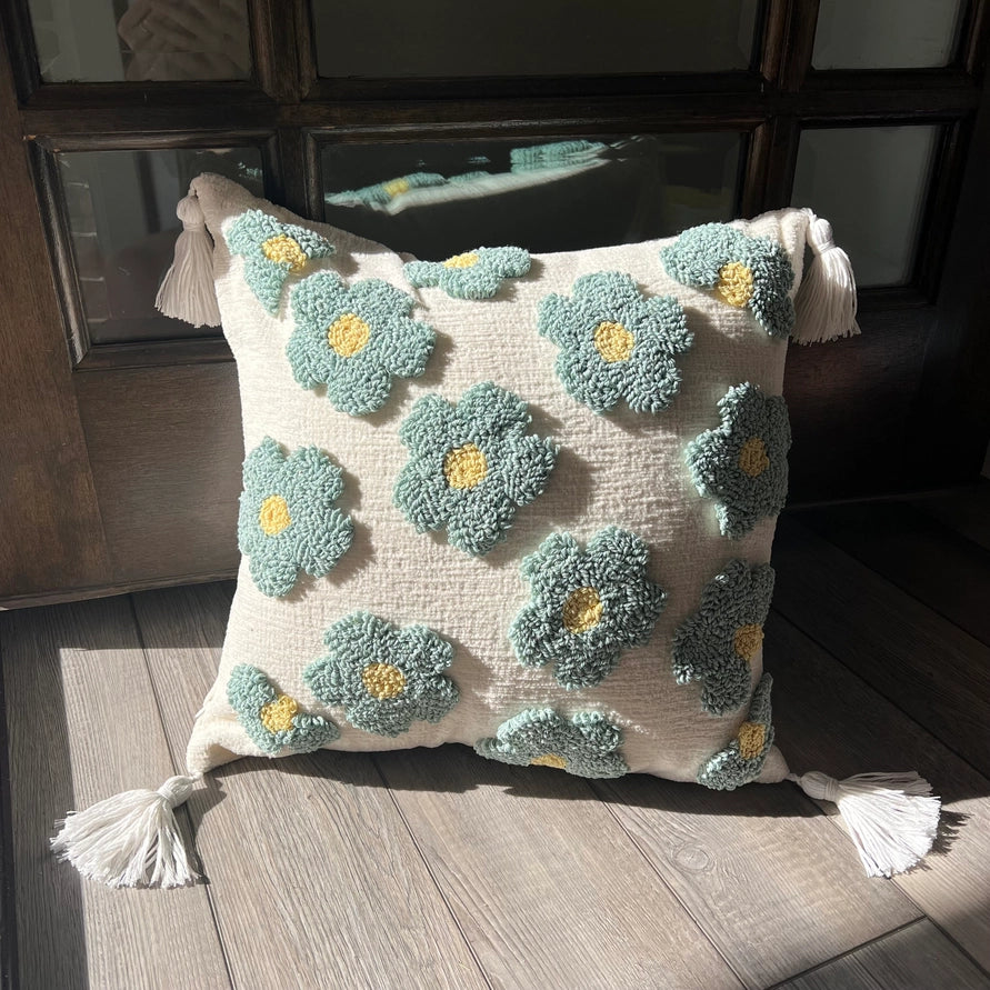 Decorative pillow with floral patterns and tassels on a wooden floor.
