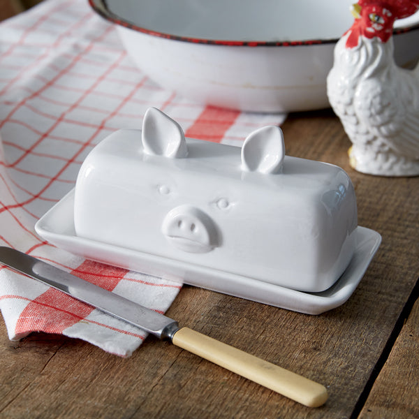 White ceramic butter dish shaped like a pig with a knife on a wooden surface.