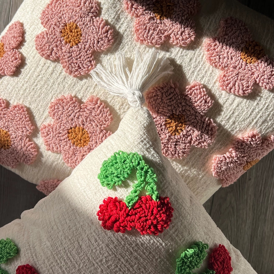 Decorative pillow with pink floral and red berry patterns on a wooden surface