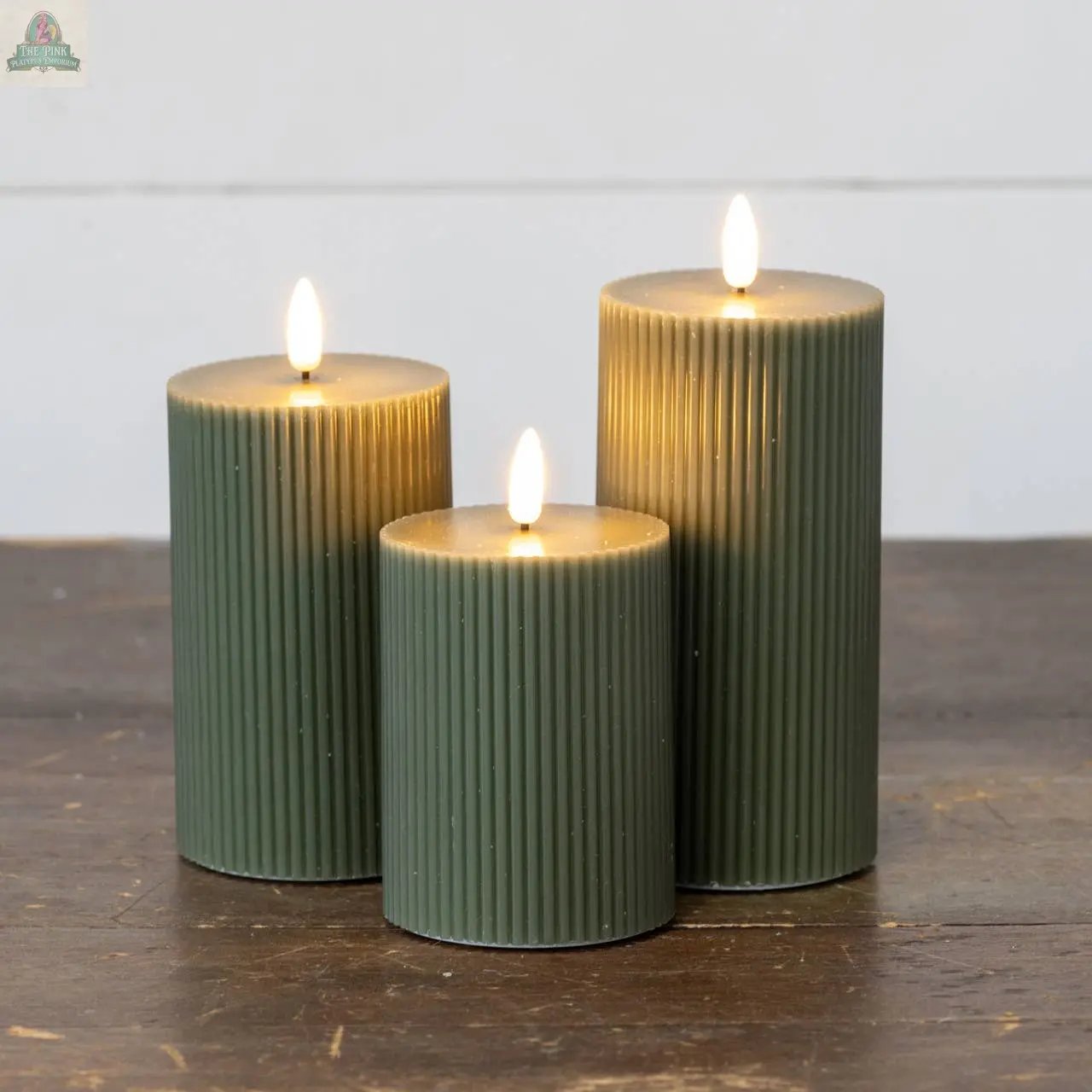 A group of Ragon House 6" Dark Green Grooved 3D Flame Candles, featuring flameless technology, are lit and arranged together on a wooden surface against a plain white background.