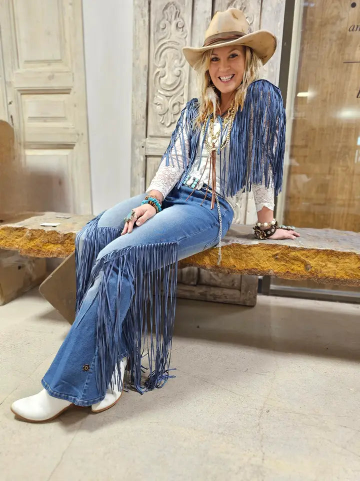 Woman wearing a blue fringe outfit with a hat, sitting on a bench.