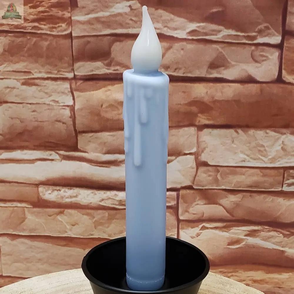 A 7" Timered Color Taper in black, featuring wax drips and a flame-shaped tip, stands upright in a sleek holder against a tan brick wall background.