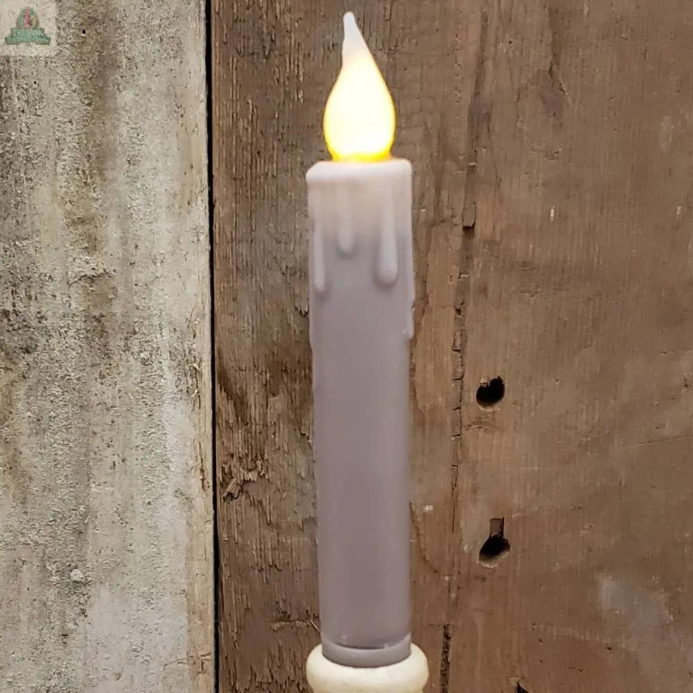 A 7" Timered Color Taper in burgundy with a glowing tip and wax-like drips stands against a rough, brown wooden background.