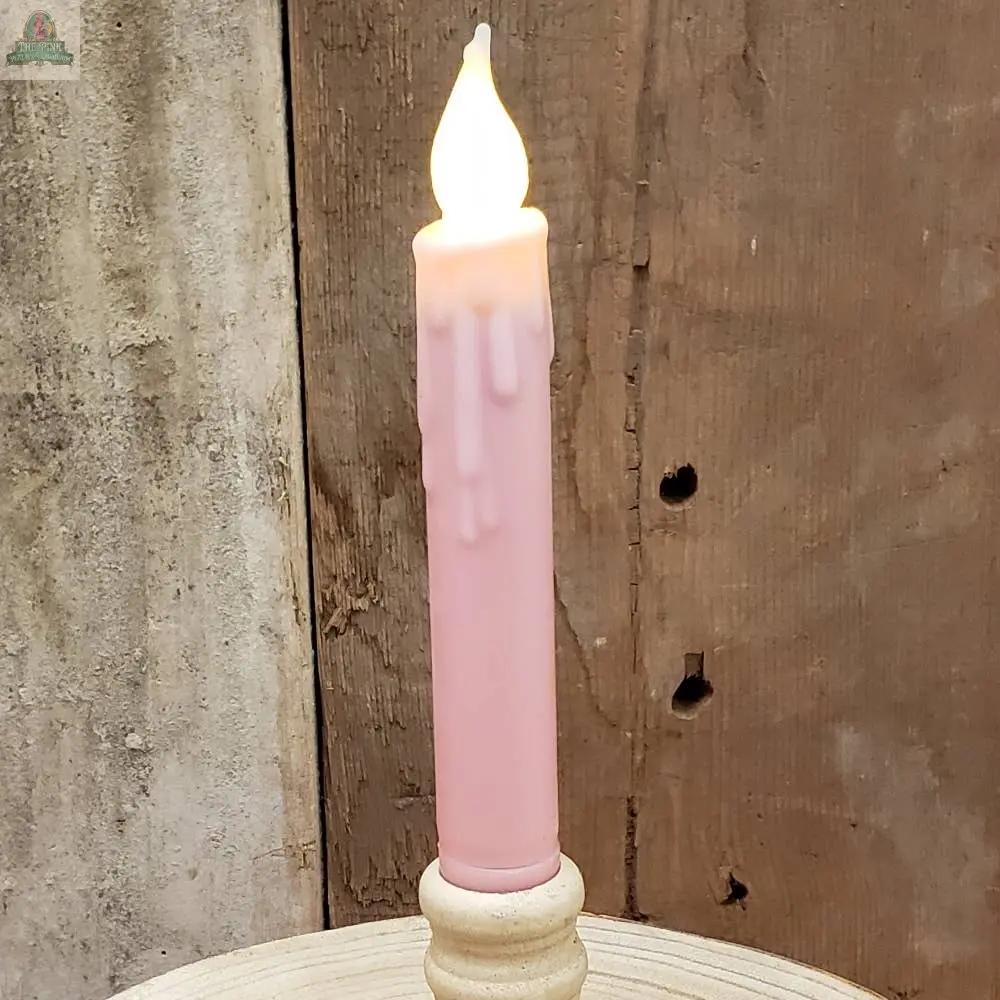 A burgundy 7-inch taper with wax drips and glowing flame rests in a cream holder on rustic wood, blending classic candle charm with the convenience of a battery-operated, timered design.