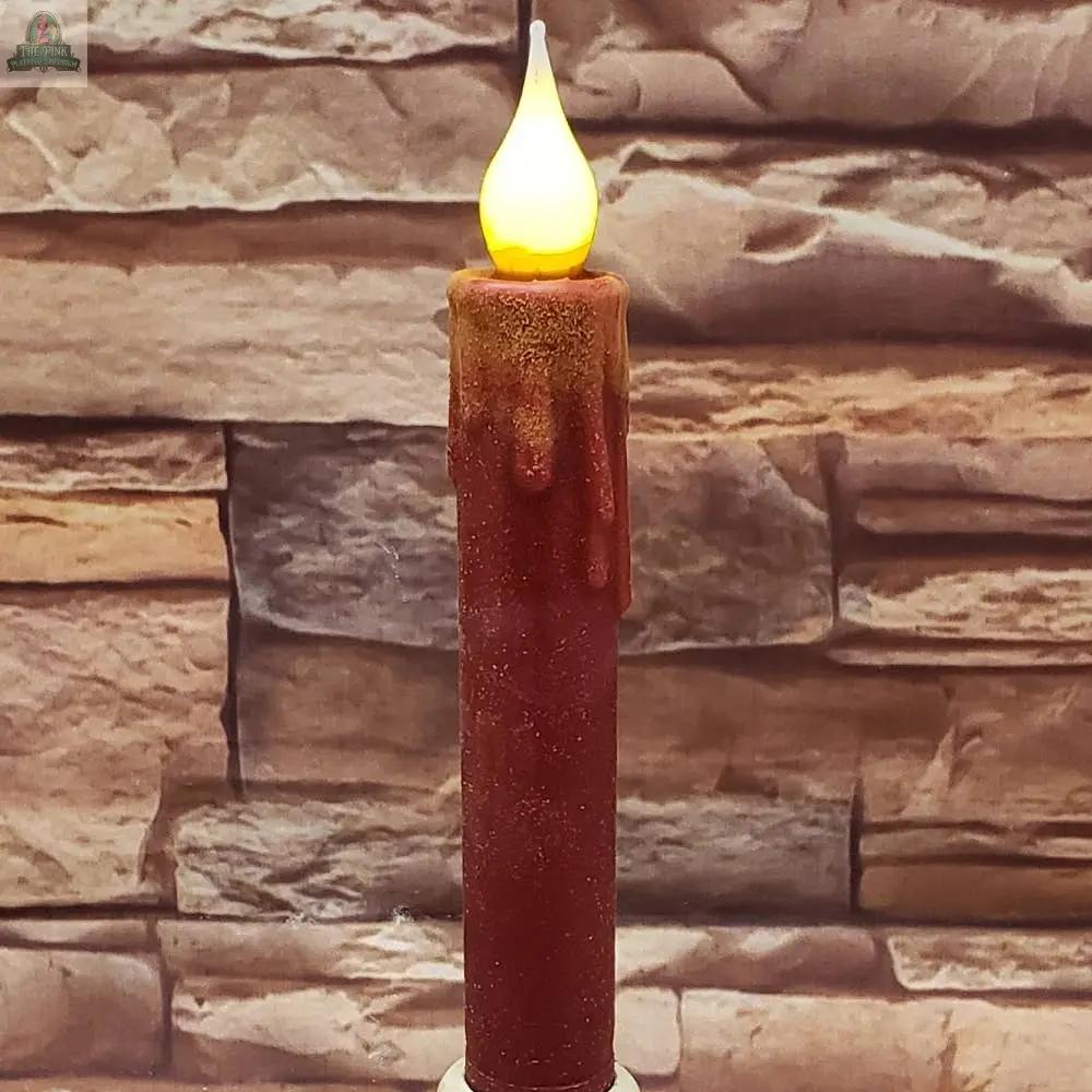 The 7" Timered Color Taper in cream, featuring artificial melted wax detail and a glowing LED flame, stands in front of a stone brick wall background.