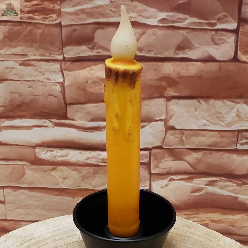 A cream 7" timered color taper with a faux melted wax look and flame-shaped tip stands upright in a small black holder against a stone-patterned background.