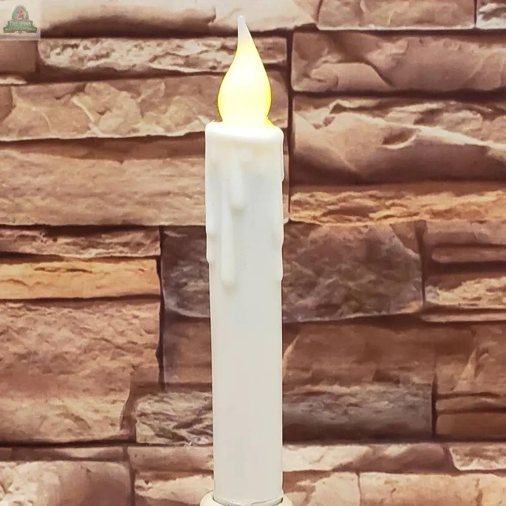 A 7" Timered Color Taper in red, featuring a glowing flame-shaped bulb and wax-like drips, stands in front of a stone-patterned wall.