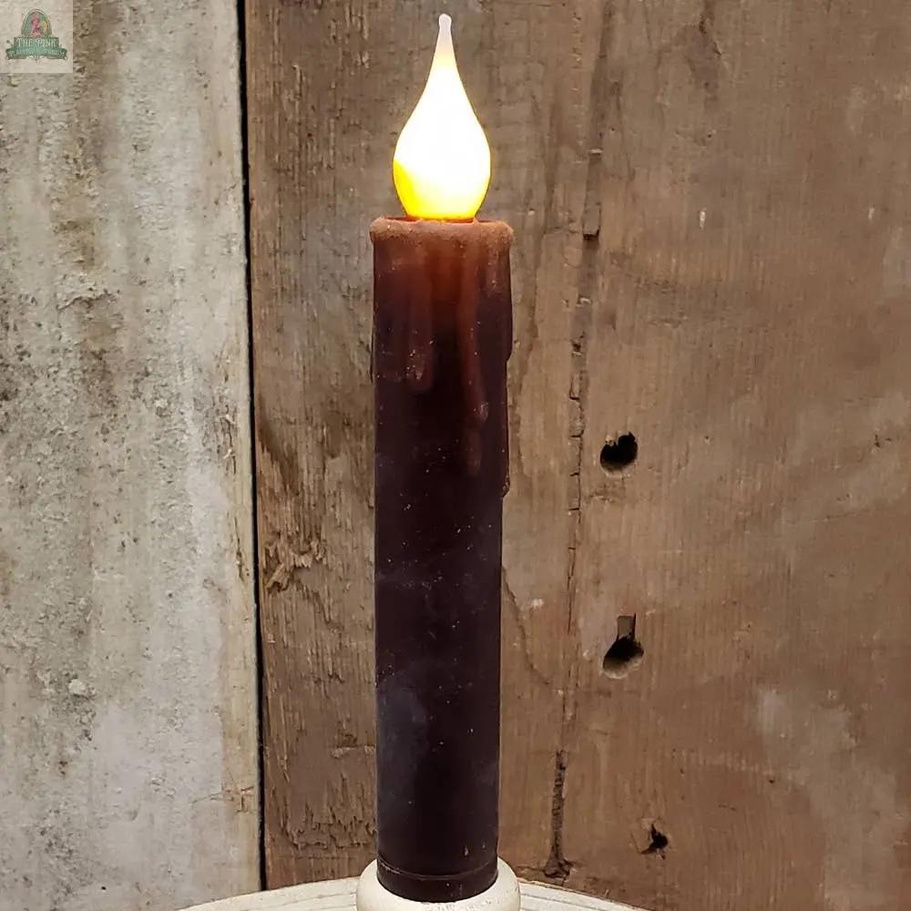 A 7" Timered Color Taper in red, featuring melted wax drips and a glowing flame, sits before a weathered wooden background.