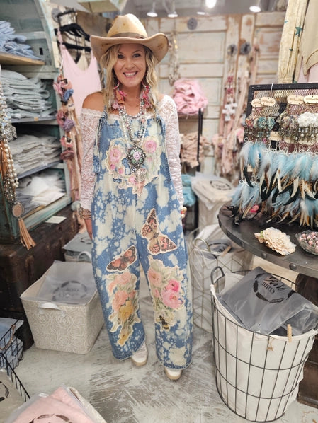 Woman wearing denim overalls with butterfly designs in a store setting.
