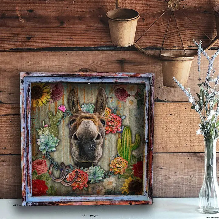 Decorative wall art with a donkey's face surrounded by flowers and cacti in a rustic frame.