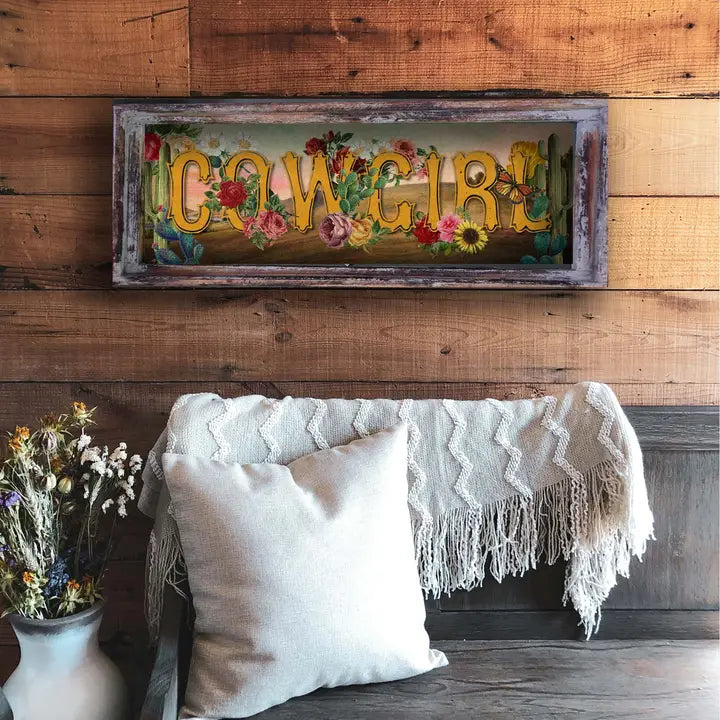 Western wall art with floral letters on a wooden wall above a sofa with pillows and a blanket.