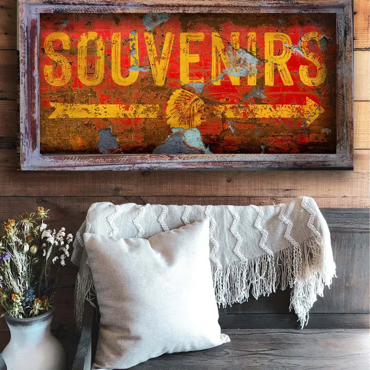 rustic wall art  with 'SOUVENIRS' text above a couch with pillows and a blanket.
