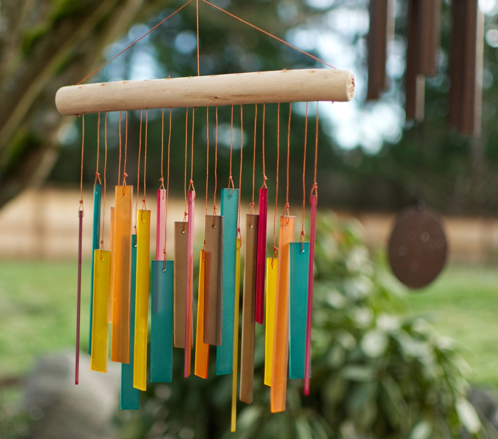 Colorful wind chime hanging outdoors with greenery in the background