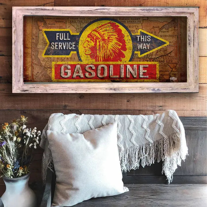Vintage-style western wall art gasoline sign framed on a wooden wall above a sofa with decorative pillows and a blanket.