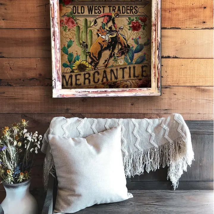 Decorative sign with 'Old West Traders Mercantile' on a wooden wall above a couch with a blanket and pillows.